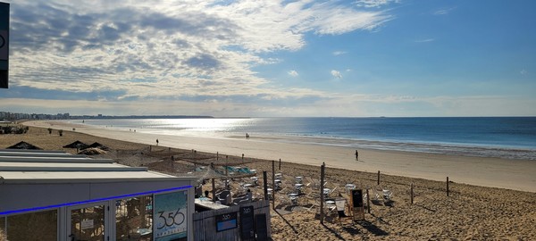 Vue panoramique de la plage de La Baule sous un ciel partiellement nuageux, avec transats et brasserie en premier plan