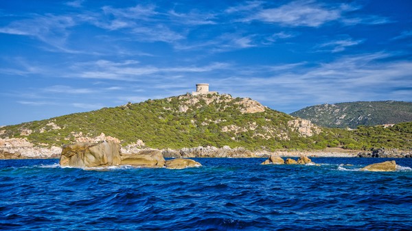 La côte de Campomoro avec ses belles eaux d’un bleu profond, vue de la mer, avec la tour de guet sur la colline au soleil