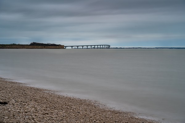 Plage de galets de mer avec des rochers et une longue passerelle dans l’eau. Plage de L’houmeau avec pont de l’île en arrière-plan