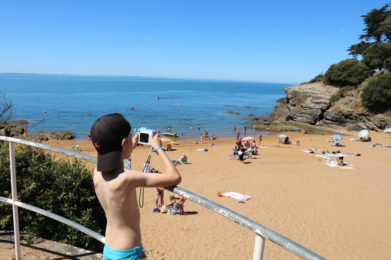 Un enfant photographie une plage de bord de mer, appareil à la main